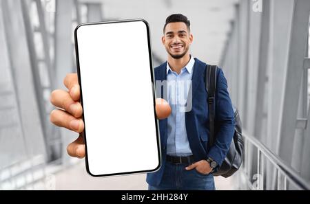 Homme arabe souriant debout à l'aéroport et montrant un smartphone vierge à l'appareil photo Banque D'Images