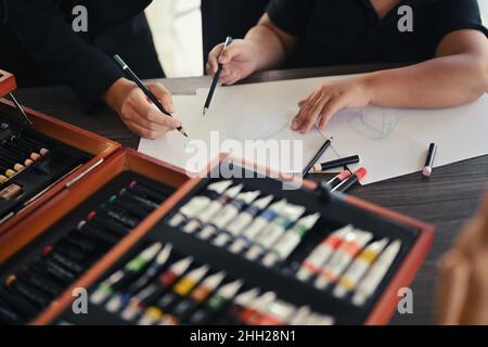 Un professeur de photographie rogné aide les enfants à dessiner des images en cours d'art. Banque D'Images