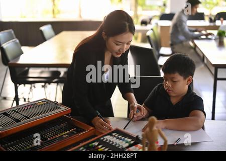 Un professeur asiatique souriant aide les enfants à colorier l'image en classe d'art Banque D'Images