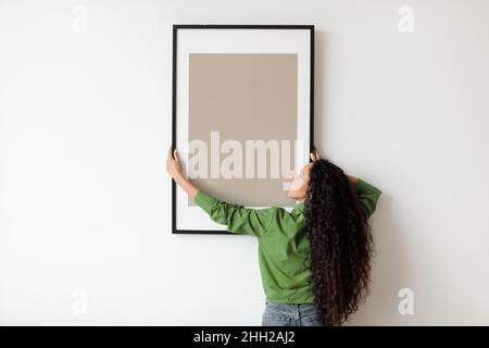 Cadre à suspendre pour femme avec affiche vide sur le mur blanc à l'intérieur Banque D'Images