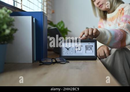 Femme souriante en chandail chaud main de réglage ou de changement de l'heure sur l'horloge. Banque D'Images