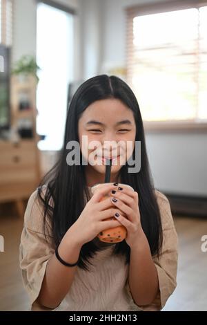 Une fille asiatique souriante boit du thé au lait glacé. Banque D'Images