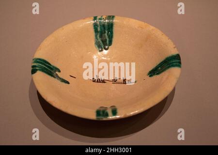 Bol aux éclaboussures vertes et inscription, 'Sovereignty is God' 9th–10th siècle en regardant ce bol trouvé à Nishapur, Iran, nous remarquons quatre éclaboussures distinctes de glaçage vert qui s'encercle du bord vers la base du bol sur le sol blanc opaque.Cette technique a été couramment utilisée dans la production de céramique dans tout l'Iraq et dans l'ouest de l'Asie centrale au neuvième et dixième siècle.L'inscription arabe noire au centre indique "Sovereignty appartient à Dieu".Bol aux éclaboussures vertes et à l'inscription, « la beauté est celle de Dieu ».9th–10th siècle.Faïence; peinte en noir avec des touches de gre Banque D'Images