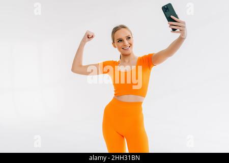 Happy sporty woman photo selfies sur smartphone et montrant les biceps isolé sur fond blanc Banque D'Images