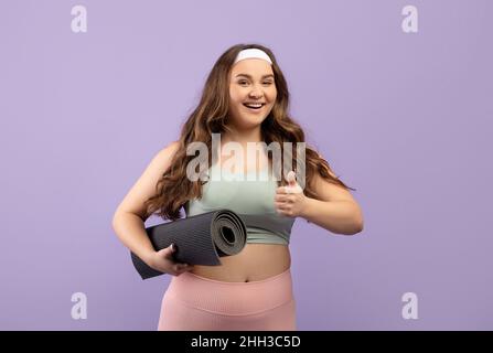 Joyeux caucasien plus taille jeune femme en uniforme de sport avec mat montrer pouce vers le haut Banque D'Images