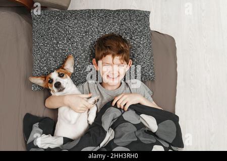 Un petit garçon heureux se trouve sur un lit avec un chien de terrier Jack russell.Concept d'enfance heureuse. Banque D'Images