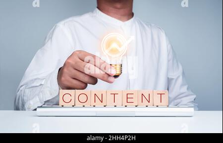 Concept de contenu, de médias numériques en ligne.CONTENU de mot sur bloc cube en bois sur ordinateur clavier avec homme d'affaires en chemise blanche tenant la lumière numérique bu Banque D'Images