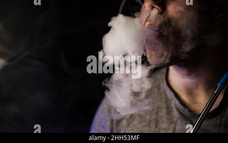 Homme fumeur, exhalle de fumée.Vapeur d'une cigarette électronique.Portrait d'un jeune homme dans la fumée.Souffle des tourbillons de vapeur.Narguilé Banque D'Images