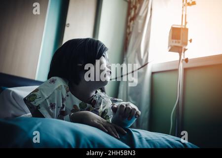 Maladie enfant asiatique admis à l'hôpital alors qu'une solution saline intraveineuse (IV) est à portée de main.Une jeune fille malheureuse déprime et désespérante, sans esprit de regarder dehors, Banque D'Images