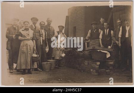 Soupe cuisine, début 20th siècle: Hommes et femmes travaillant à côté d'une gamme de cuisine extérieure avec de grandes casseroles.Un homme a une grande louche, une femme porte un panier, et deux seaux sont sur le sol Banque D'Images