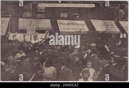 Polly Nathan's Fish shop, Petticoat Lane, début du 20th siècle : grande foule dans la rue (hommes, femmes et enfants). Un panneau pour 'Polly Nathan, Fish Dinners' est en arrière-plan. Une affiche pour une vente par F. Littman & Company est également exposée Banque D'Images