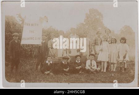 'Débarque avec jour de lavage' : groupe d'enfants dans un champ, rassemblés autour de trois baignoires de lavage.Deux garçons tiennent une bannière qui dit « le jour du lavage », début du 20th siècle Banque D'Images