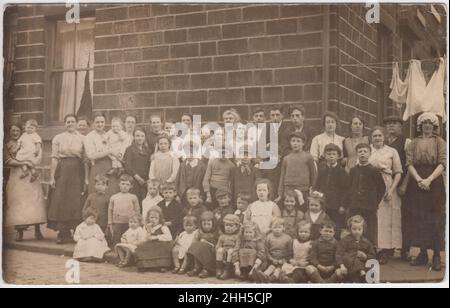 Les familles d'une rue de classe ouvrière posant à l'extérieur pour un photographe, début 20th siècle.Les gens à la maison étaient surtout des femmes et des enfants, les vêtements sur une ligne de lavage peuvent être vus en arrière-plan Banque D'Images