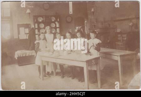 Les filles étant enseignées à cuisiner dans une cuisine scolaire, début du 20th siècle.L'équipement de blanchisserie peut être vu en arrière-plan, y compris une mangle Banque D'Images