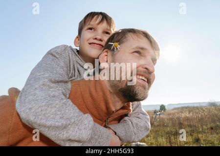 Un père donne une promenade en pigeyback à son fils par beau temps Banque D'Images