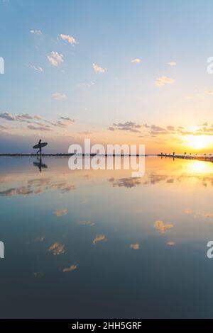 Silhouette d'homme marchant avec planche de surf à la plage avec réflexion Banque D'Images