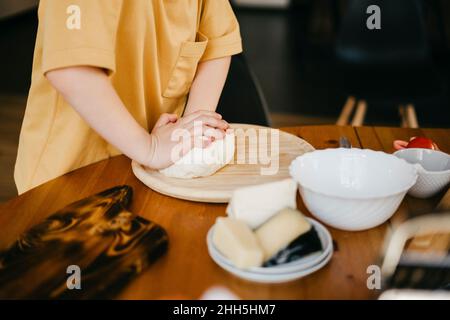 Garçon pétriant de la pâte à pizza sur une table à la maison Banque D'Images