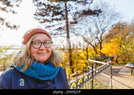 Femme âgée souriante écoutant de la musique à l'aide d'un casque sans fil dans le parc Banque D'Images