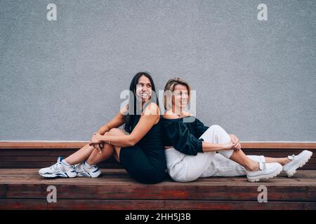 Des amis souriants assis dos à dos sur le banc devant le mur Banque D'Images