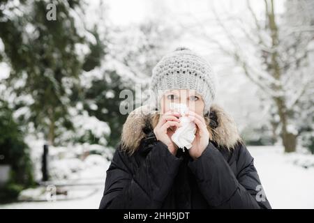 Femme soufflant le nez avec des mouchoirs dans le parc d'hiver Banque D'Images