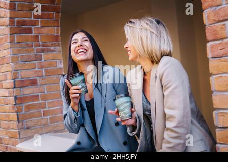 Des amies gaies qui apprécient le café assis ensemble au mur Banque D'Images