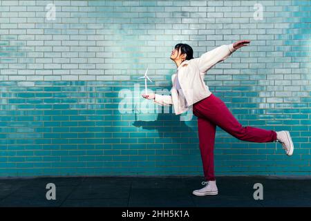 Femme avec l'équilibre de jouet d'éolienne sur une jambe par mur de brique turquoise Banque D'Images