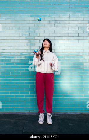 Jeune femme jonglant avec de petits globes devant le mur de briques turquoise Banque D'Images