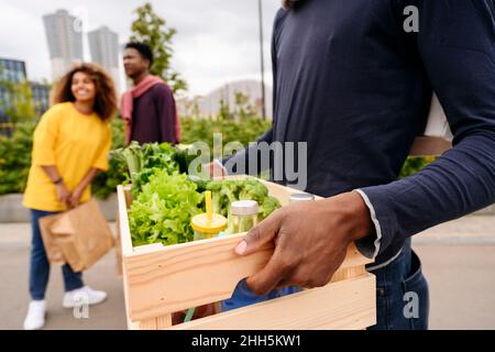 Homme portant un panier de légumes et d'amis en arrière-plan dans la rue Banque D'Images