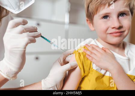 Infirmière avec un gant de protection et un masque vaccinant le garçon au centre Banque D'Images
