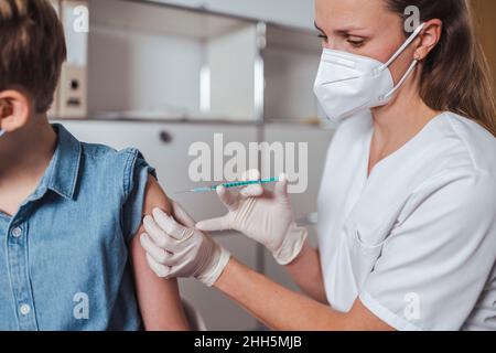 Travailleur de la santé sous masque facial administrant le vaccin COVID-19 au garçon Banque D'Images