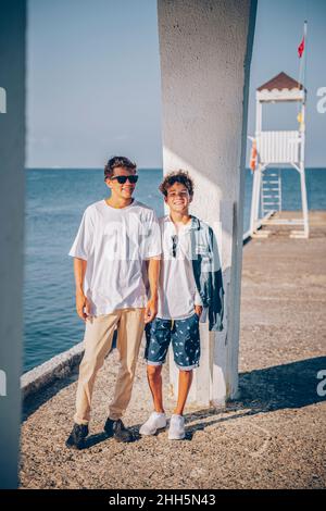 Des frères souriants se tenant sur la jetée en face de la mer Banque D'Images