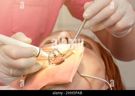 Une patiente avec un écarteur de joue avec un cercueil vert dans une clinique dentaire, un dentiste en gants de latex examine ses dents avec un bore et un miroir, a Banque D'Images