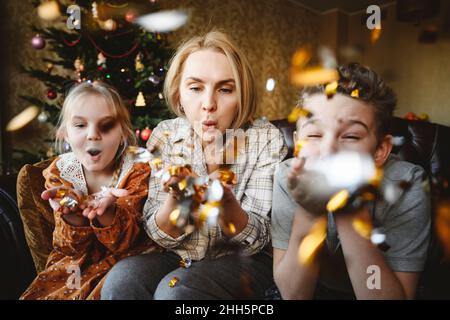 Mère avec fille et fils soufflant confetti à la maison Banque D'Images