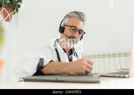 Médecin avec un casque écrivant sur une planchette à pince au bureau à domicile Banque D'Images