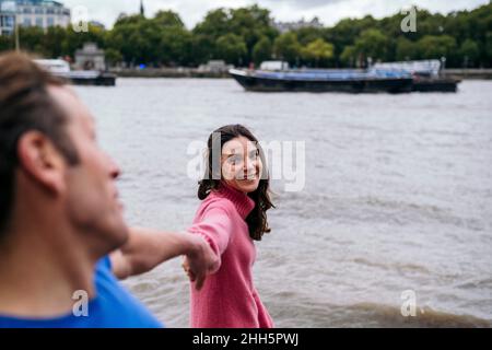 Femme souriante tenant les mains de l'homme au bord de la rivière Banque D'Images