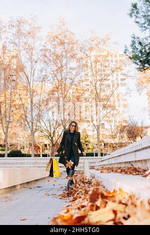 Femme avec des sacs de shopping marchant au-dessus des feuilles d'automne tombées sur le sentier Banque D'Images
