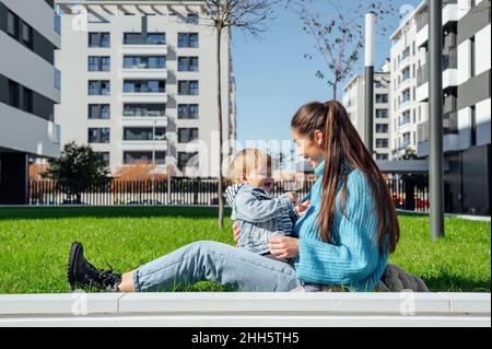 Mère gaie jouant avec son fils sur l'herbe dans la ville Banque D'Images