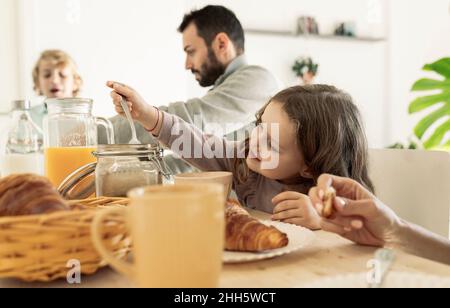 Fille tenant une cuillère sur un pot à la table du petit déjeuner Banque D'Images