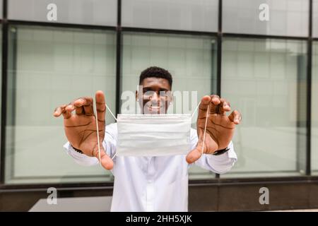 Homme souriant montrant un masque chirurgical devant le mur Banque D'Images