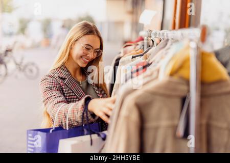 Une femme souriante magasiner des vêtements disposés sur un porte-vêtements à l'extérieur du magasin Banque D'Images