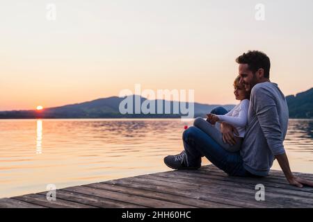 Jeune fille souriante assise sur les genoux de son père au bord du lac, Mondsee, Autriche Banque D'Images