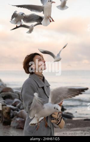 Femme réfléchie au milieu de mouettes volantes à la plage Banque D'Images