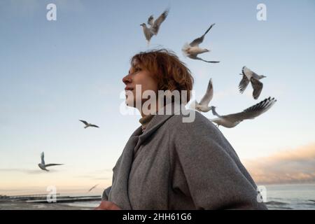 Femme attentionnés en volant mouettes au coucher du soleil Banque D'Images