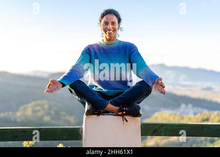 Femme souriante assise en position lotus sur une rampe au parc Banque D'Images