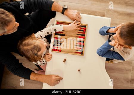 Grand-père jouant du backgammon sur la table avec des petits-enfants à la maison Banque D'Images