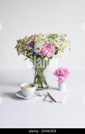 Studio tourné d'une tasse de café et d'un bouquet de pivoines, de féverfews (Tanaceum parthenium), de fleurs de tournesol (Campanula) et de lacéflowers blancs (Orlaya grandiflora) Banque D'Images