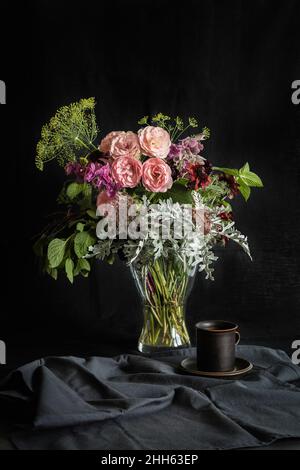 Studio photo d'une tasse de café et bouquet de roses Mini Eden, des journaux annuels (Salvia viridis), de la dentelle Queen Annes (Daucus carota), des Susans à yeux noirs (Rudbeckia hirta), du ragwort d'argent (Jacobaea maritima), de la menthe et de l'aneth Banque D'Images