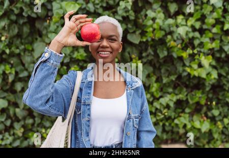 Femme couvrant l'œil avec une pomme debout devant la plante Banque D'Images