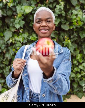 Jeune femme avec sac en maille tenant la pomme devant les plantes Banque D'Images