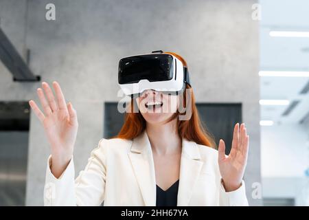 Femme de travail excitée portant le simulateur de réalité virtuelle gestant avec la bouche ouverte au bureau Banque D'Images